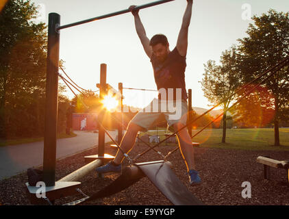 Silhouetted young man swinging on playground climbing frame at sunset Stock Photo