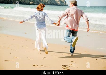 Mature couple holding hands running on beach, Camaret-sur-mer, Brittany, France Stock Photo