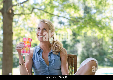 Mature woman sitting in garden with drink Stock Photo