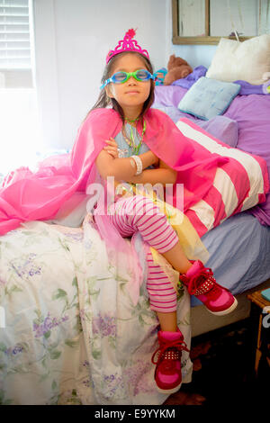 Young girl wearing fancy dress costume, sitting on bed