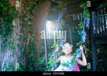 Young girl wearing fancy dress costume, sitting on tree swing Stock Photo