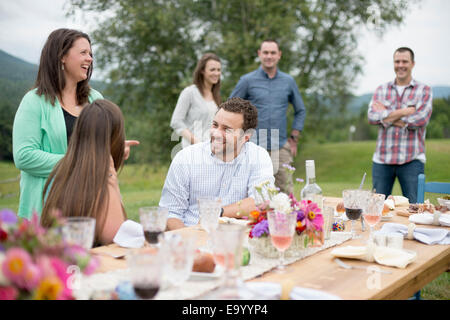 Family and friends gathered around, talking, at the end of a meal, outdoors Stock Photo