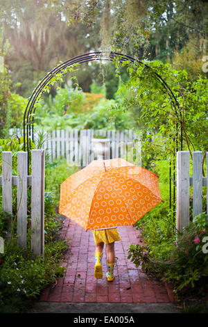 Girl walking through garden gate carrying umbrella Stock Photo
