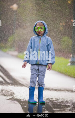 Portrait of boy wearing scuba goggles and rubber boots standing in street puddle Stock Photo