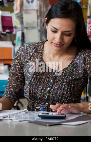 Female sales assistant using calculator in stationery shop Stock Photo