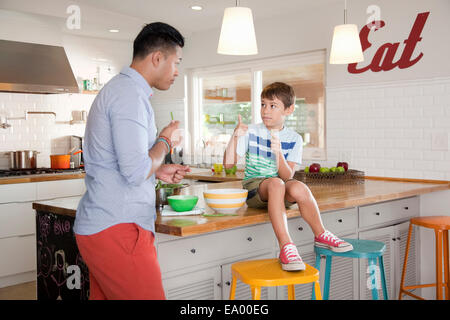 Father and son in kitchen, boy sitting on counter