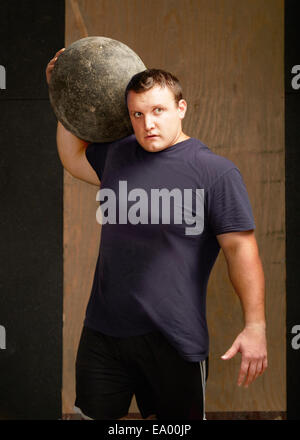 Portrait of young male weightlifter with atlas ball on shoulder in gym Stock Photo
