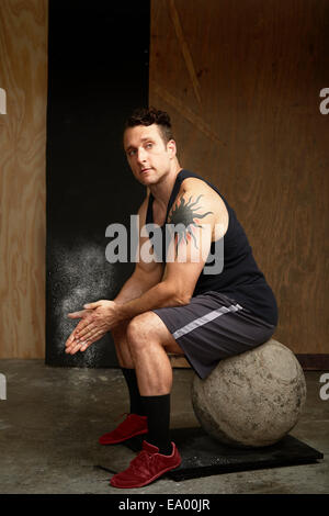 Portrait of mid adult man sitting on atlas ball in gym