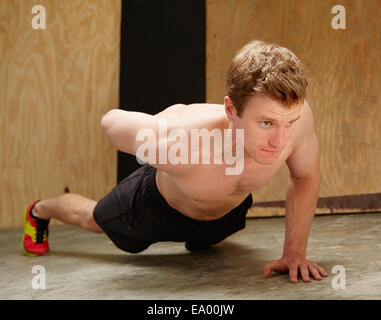 Mid adult male doing one armed push ups in gym Stock Photo