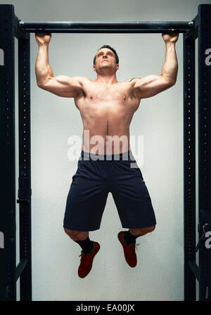 Mid adult male doing pull ups on exercise bar in gym Stock Photo