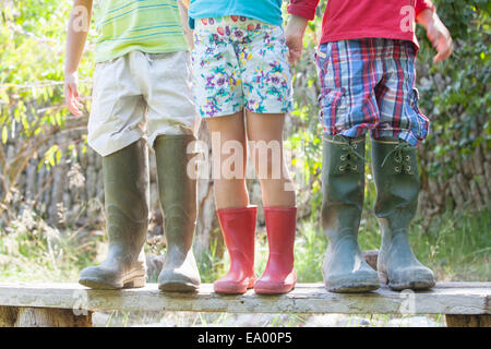 Three children on garden seat in over sized rubber boots Stock Photo
