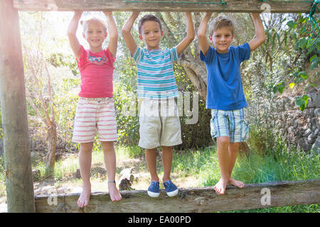 Three children in garden standing on fence Stock Photo