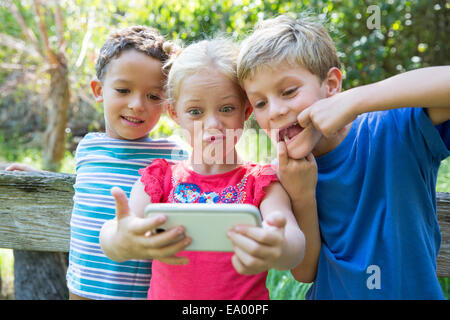 Three children in garden taking selfie on smartphone Stock Photo