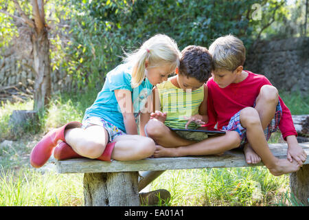Three children sitting on garden seat looking down at digital tablet Stock Photo