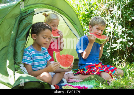 Three children eating watermelon slices in garden tent Stock Photo
