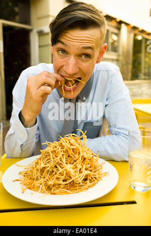 Young man eating skinny french fries at sidewalk cafe Stock Photo