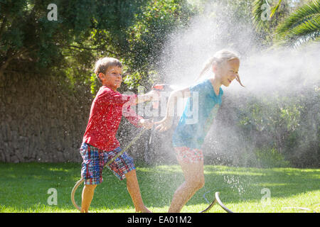 Boy splashing girl in garden with water sprinkler Stock Photo