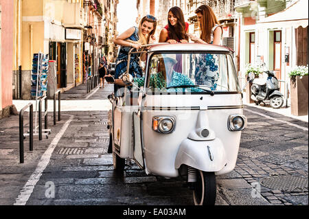 Three young women standing up in open back seat of Italian taxi, Cagliari, Sardinia, Italy Stock Photo