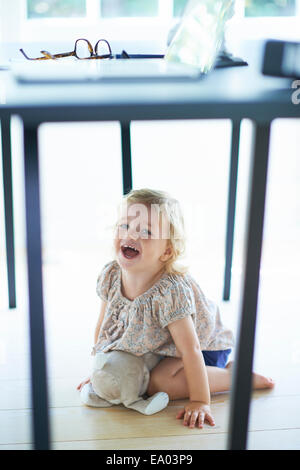 Female toddler hiding and laughing under dining room table Stock Photo