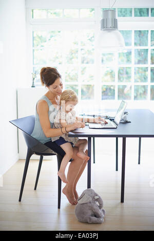Mid adult woman and toddler daughter typing on laptop Stock Photo