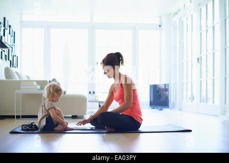 Mid adult mother and toddler daughter practicing yoga in living room Stock Photo