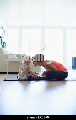 Mid adult mother and toddler daughter practicing lotus position in living room Stock Photo