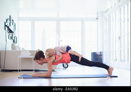 Mid adult mother practicing yoga with toddler daughter on top of her Stock Photo