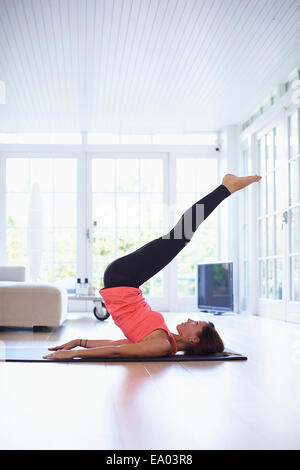 Mid adult woman lying on back practicing yoga in living room Stock Photo