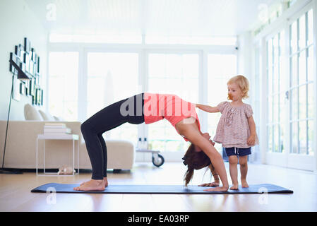 Mid adult mother practicing yoga with curious toddler daughter Stock Photo