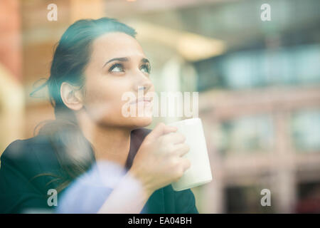 businesswoman drinking coffee and looking out of cafe window, London, UK Stock Photo