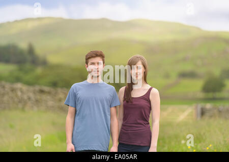 Young couple standing together in meadow and looking away over rural landscape Stock Photo