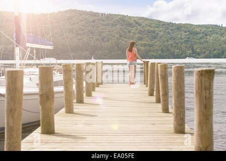 Young woman standing on jetty looking over lake on sunny day Stock Photo