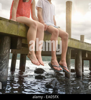 Young couple holding hands together and sitting on edge of jetty over lake Stock Photo