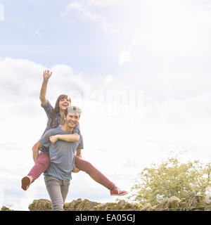 Young man giving piggyback ride to girlfriend in countryside under bright sunny sky