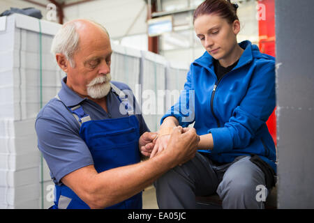 Factory worker applying first aid to colleague Stock Photo