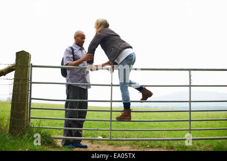 Couple climbing over gate in fields Stock Photo