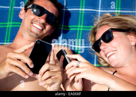 Young couple lying on beach towel using smartphones Stock Photo