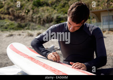 Young adult male surfer waxing board