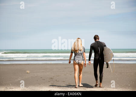 Young couple walking out to sea, young man carrying surfboard