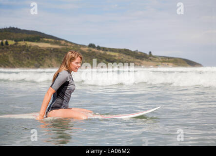 Portrait of young woman sitting on surfboard in sea