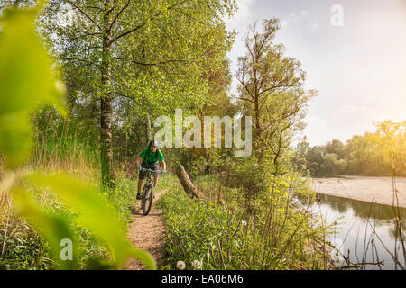Young man cycling along riverside path