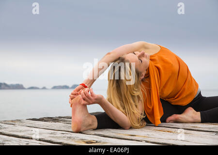Mid adult woman touching toes practicing yoga on wooden sea pier Stock Photo