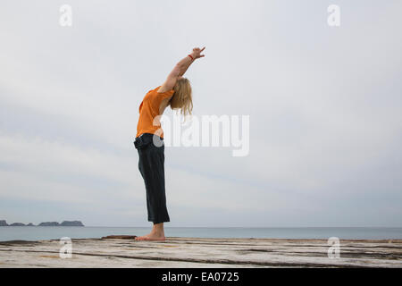 Mid adult woman stretching back practicing yoga on wooden sea pier Stock Photo
