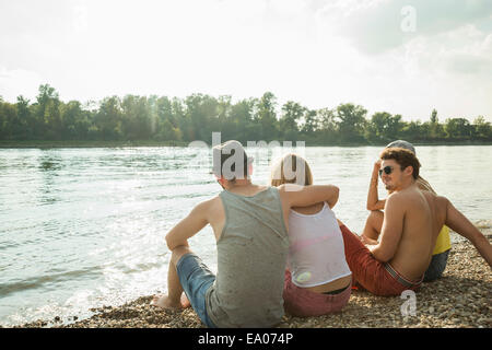 Four young friends sitting on lakeshore Stock Photo