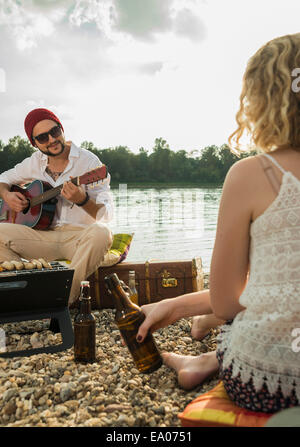 Young man sitting by lake playing guitar Stock Photo
