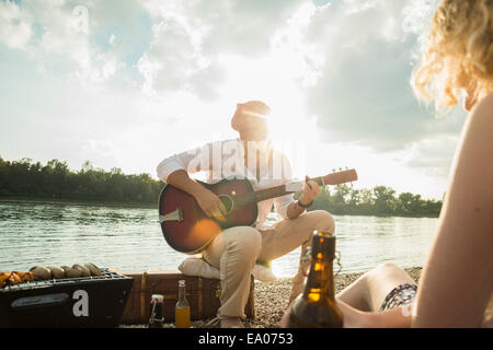 Young man sitting by lake playing guitar Stock Photo