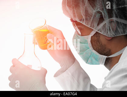 Chemist pouring liquid from beaker into flask Stock Photo