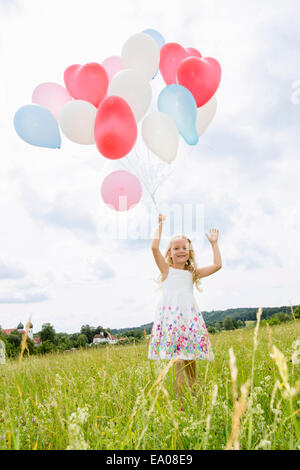 Girl holding balloons in field Stock Photo