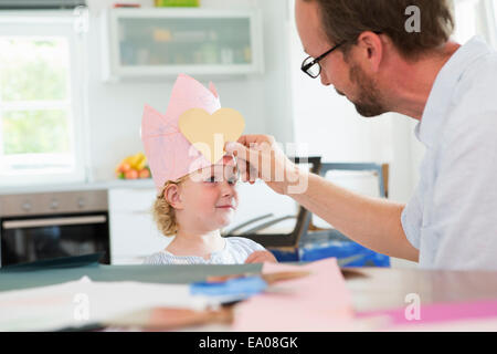 Father putting heart shape on daughter's paper crown Stock Photo