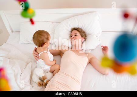 Mother and baby daughter lying on bed, high angle